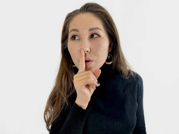 Uzun kahverengi saçlı, güzel Asyalı bir kadının izole edilmiş beyaz arka planda dudaklarına parmak atması ön planda. 