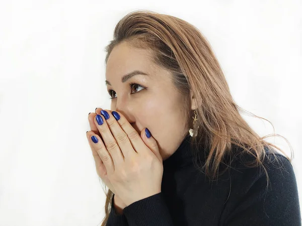 Uzun kahverengi saçlı, genç ve güzel Asyalı kadının bakışları düşünceli bir şekilde başka yöne bakıyor ve ağzını avuç içiyle kaplıyor.