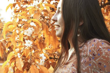 Bahçedeki sarı ağacın yanındaki parlak dişli tebessümle uzun saçlı mutlu Asyalı kadının yan görüntüsü. 