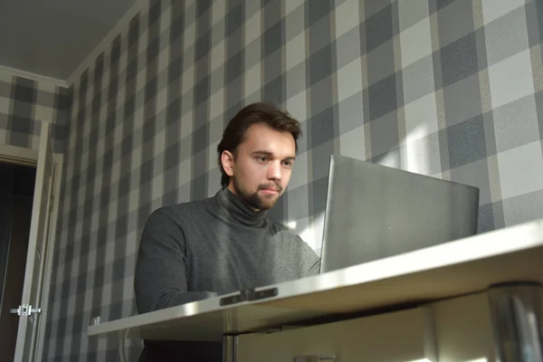 Genç, yakışıklı, sakallı, serbest çalışan erkek bilgisayarın altında güneş ışığı altında bilgisayarla çalışıyor.