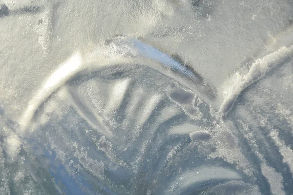 Long thin snaking lines of patterns on transparent frozen ice sculptures in park in wintertime in sunlight