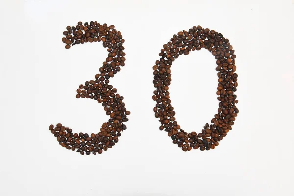 Beyaz arka plandaki lambalar ışığında bir sürü küçük koyu kahverengi kahve çekirdeğinden yapılmış büyük 30 nubmer 'ın üst görüntüsü