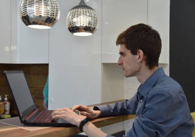 Tanımlanamayan genç, sıska erkek serbest çalışan dizüstü bilgisayar kullanarak rahat bir dairede lambalar ışığında proje yapıyor.