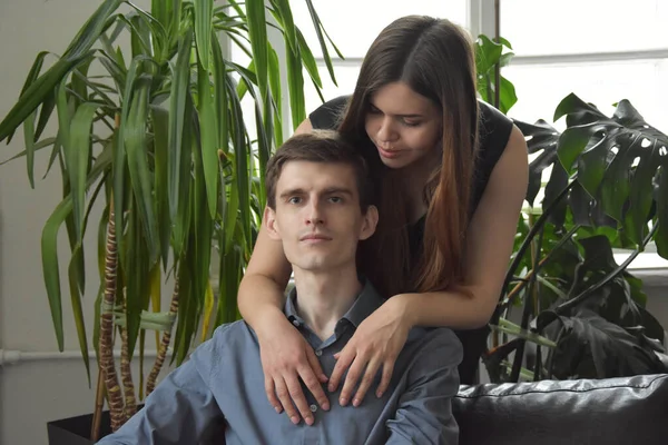 Mavi gömlekli, mutlu, genç bir adamın önünde gülümseyen bir kameraya bakarken güzel bir kadın onu kucaklıyor.