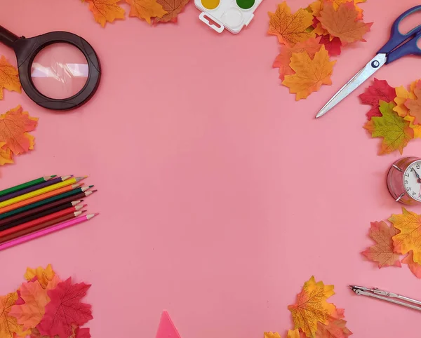 Okul malzemelerinin yukarısından seçici odak noktası örneğin büyüteç ve saat ve pembe arka planda çok renkli boya kalemleri gibi. 