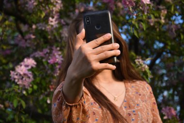 Gündüz vakti bahçede selfie çeken tanınmamış genç bir kadın. 