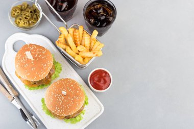 Çift peynirli burger, karamelli soğan, marul ve jalapeno, patates kızartması ve soda ile servis edilmiş, beyaz tabakta, yatay, fotokopi alanı, üst manzara.