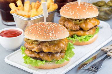 Çift peynirli burger, karamelli soğan, marul ve jalapeno, patates kızartması ve soda ile servis ediliyor, beyaz tabakta, yatay olarak.