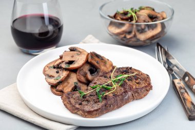 Sotelenmiş kahverengi mantarlı biftek fileto ve kekik, gri arka planda, yatay.