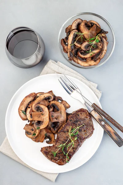 Beef steak with sauteed brown mushrooms and thyme, on a gray background, vertical, top view