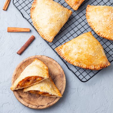 Küçük şeftali ve tarçınlı, hamur hamurlu el pastaları, şeker serpilmiş, ahşap bir tabakta ve soğutma rafında, üst manzara, kare format