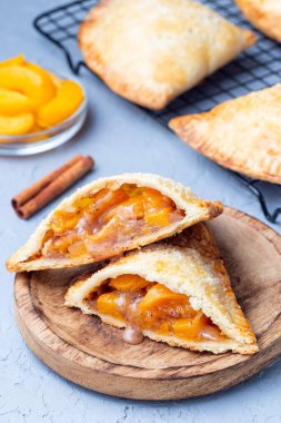 Ev yapımı küçük şeftali ve tarçınlı el turtası, hamur hamuru, şeker serpiştirilmiş, ahşap bir tabakta ve soğutma rafında, dikey