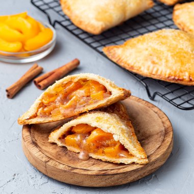 Küçük şeftali ve tarçınlı, hamur hamurlu, şeker serpilmiş, ahşap tabakta ve soğutma rafında, kare biçiminde.