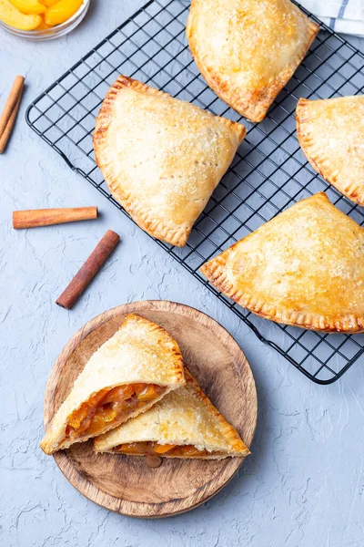 Ev yapımı küçük şeftali ve tarçınlı el turtası. Hamur hamuru, şeker serpiştirilmiş. Tahta bir tabakta ve soğutma rafında.