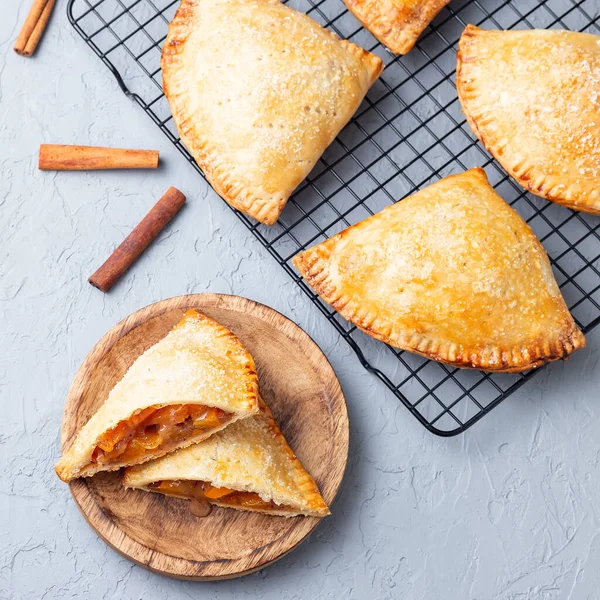 Küçük şeftali ve tarçınlı, hamur hamurlu el pastaları, şeker serpilmiş, ahşap bir tabakta ve soğutma rafında, üst manzara, kare format