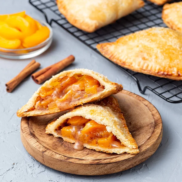 Küçük şeftali ve tarçınlı, hamur hamurlu, şeker serpilmiş, ahşap tabakta ve soğutma rafında, kare biçiminde.