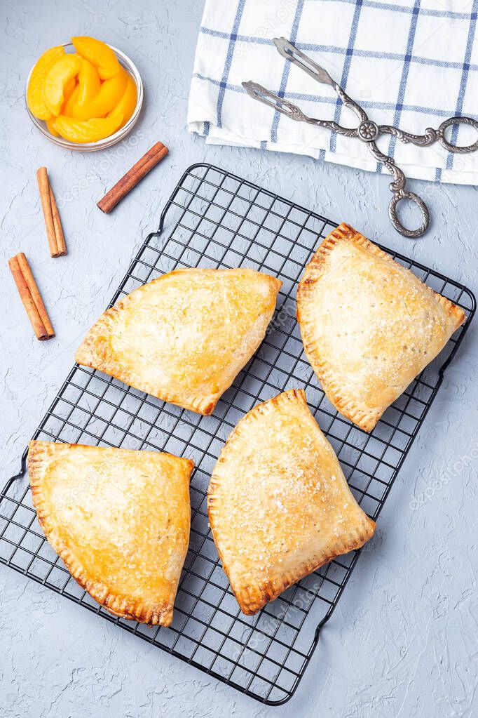 Homemade small peach and cinnamon hand pies with crust dough,  sprinkled with sugar, on a cooling rack, vertical, top view