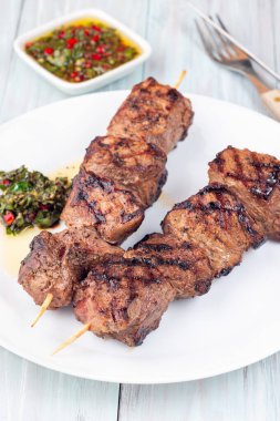Beyaz tabakta ızgara sığır filetosu ya da chimichurri soslu biftek şişi.