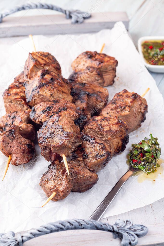 Beef meat skewers with chimichurri sauce, on a wooden tray, vertical
