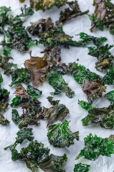 Easy three ingredient baked green kale chips with sea salt and olive oil, on a parchment, vertical