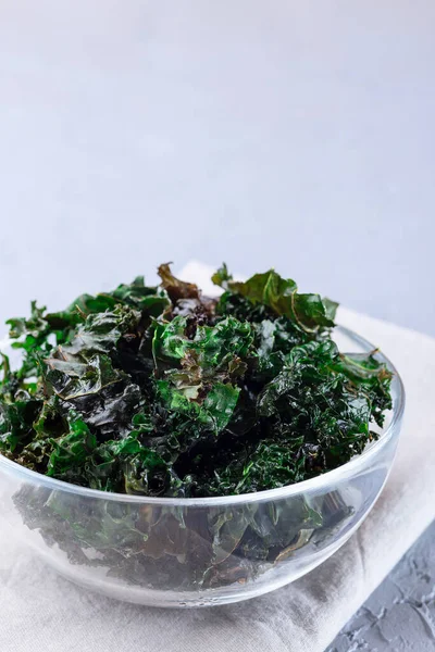 Three ingredient baked green kale chips with sea salt and olive oil, in a glass bowl, vertical, copy space