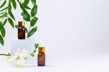 Beyaz podyumlu kahverengi cam pipet şişeleri, çiçekler ve yeşil yapraklar. Organik, sıfır atık eko cam kapta doğal kozmetik. Yatay, boşluğu kopyala