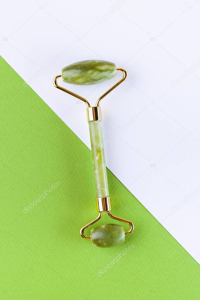 Green jade facial roller and massage on colorful background, vertical, top view. Spa cosmetics for body and face, home skin care concept