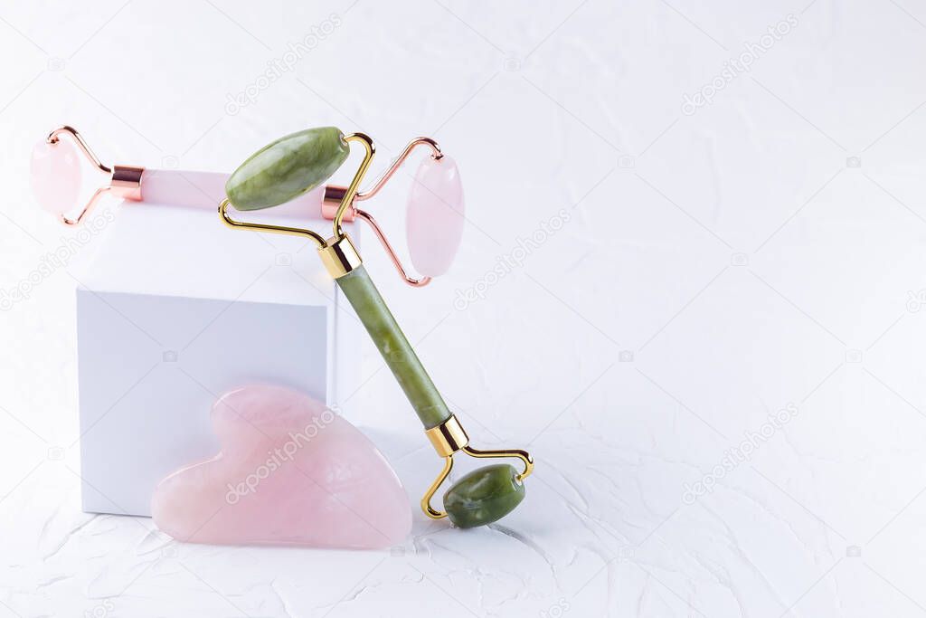Rose quartz crystal and jade facial roller and massage tool Gua sha on white background, horizontal, copy space. Spa cosmetics for body and face, home skin care concept