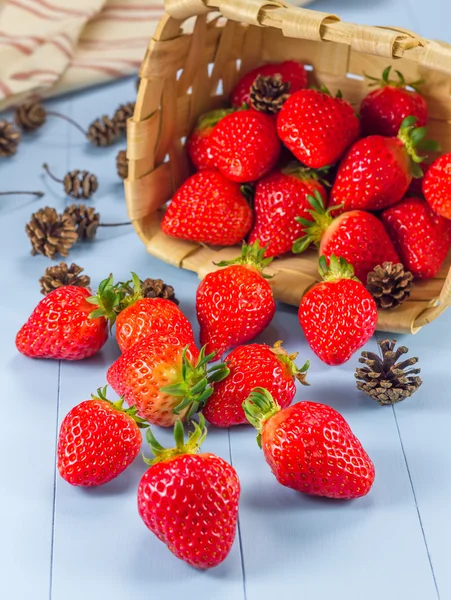 Panier avec des fraises et des cônes de sapin renversés sur une table — Photo