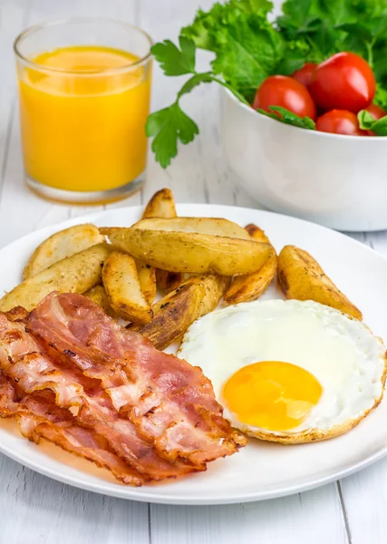 Desayuno abundante con tocino, huevo frito, papa y un vaso de jugo de naranja — Foto de Stock
