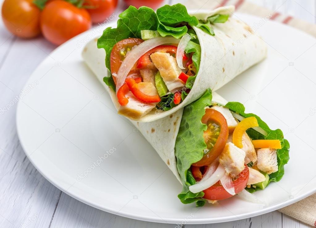 Tortilla wraps with roasted chicken fillet, fresh vegetables and sauce on white plate