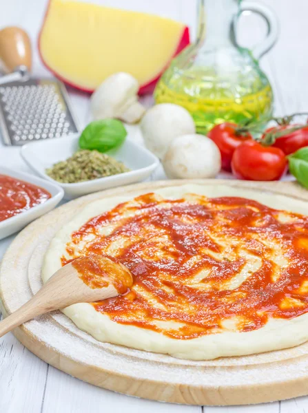 Pasta per pizza con salsa di pomodoro su una tavola di legno — Foto Stock