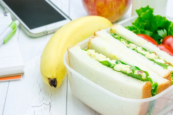 Коробка с бутербродами с яичным салатом, фруктами, молоком и канцелярскими принадлежностями — стоковое фото