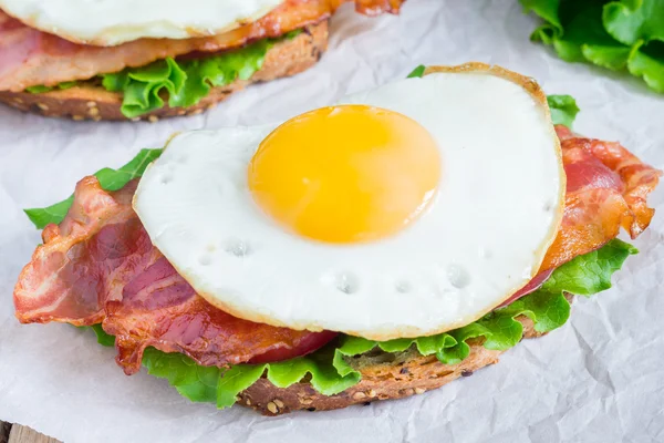 Sandwich deschis cu ou, slănină, roșii și salată verde — Fotografie, imagine de stoc