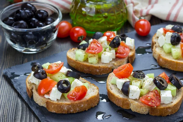 Кростини в греческом стиле с сыром фета, помидорами, огурцом, оливками и травами — стоковое фото