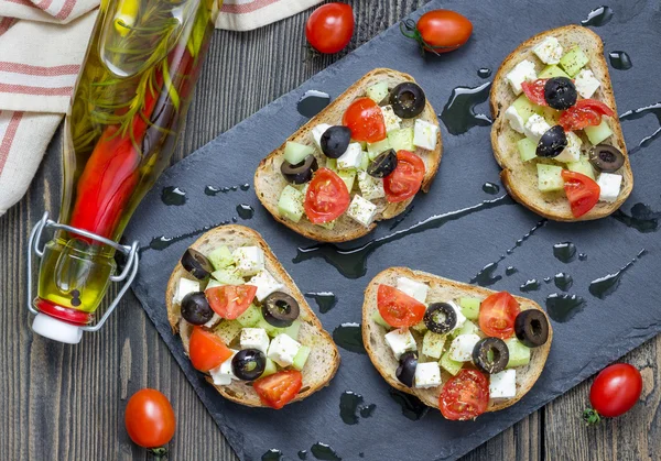 Styl grecki crostini z serem feta, pomidory, ogórek, oliwki i ziół, widok z góry — Zdjęcie stockowe