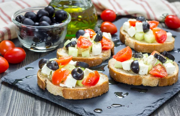 Griekse stijl crostini met fetakaas, tomaten, komkommer, olijven en kruiden — Stockfoto