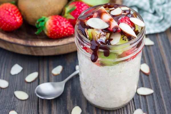 Nuit de flocons d'avoine avec fraise fraîche et kiwi, garnis de sauce au chocolat et tranches d'amande dans un bocal en verre — Photo