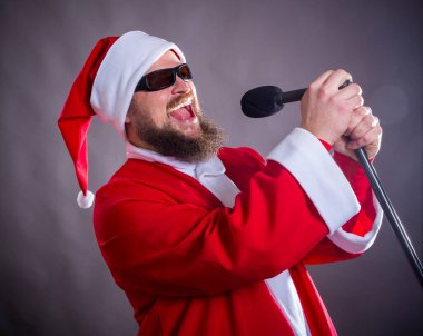 Bearded rocke with micriphome dressed in Santa Claus costume clipart