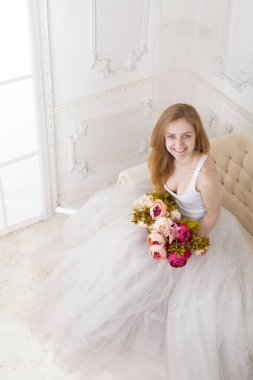 Çiçekleri olan, geniş etekli beyaz elbiseli güzel bir kadın kanepede oturuyor.