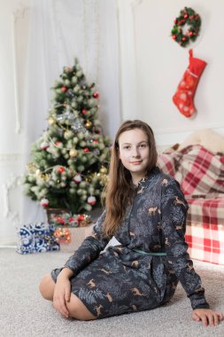 Güzel genç kız Noel ağacının önünde oturuyor.