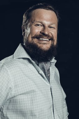 Siyah arka planda gülümseyen, gömlekli, sakallı adam..