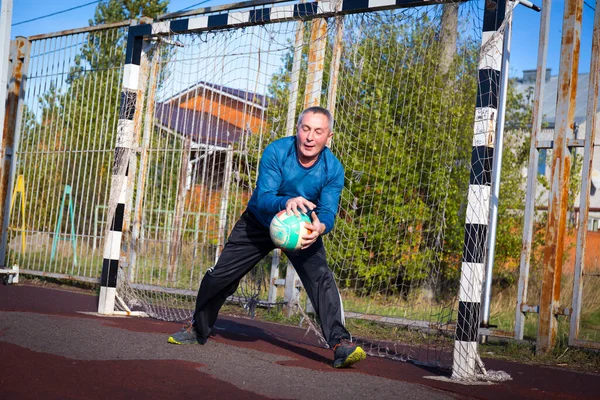 Homem idoso ativo jogando futebol em campo de esportes. — Fotografia de Stock