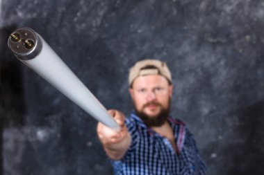 Sıradan kıyafetler giyen, floresan lambalı katı sakallı bir adam sopa gibi görünüyor.