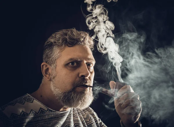 Solider bärtiger Mann, der Pfeife raucht Studio Porträt auf schwarzem Hintergrund. — Stockfoto