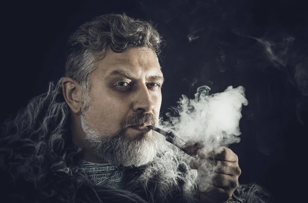Solid bearded man in a fur mantle smoking pipe