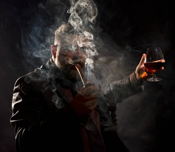 Solid confident bearded man in suit with glass of whisky smoking pipe — Stock Photo, Image