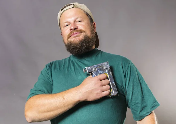 Fröhlicher bärtiger Handwerker im grünen T-Shirt, der Spaß an der Waffe hat — Stockfoto