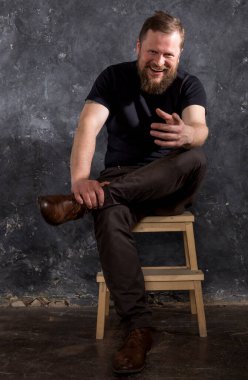 Tişört giymiş, sandalyede oturan olgun sakallı adam.