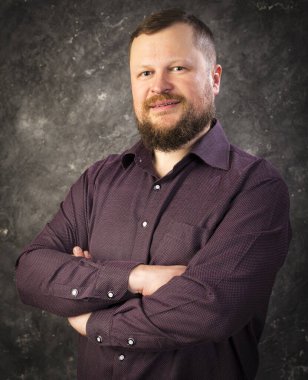 Tişörtlü sakallı adam elleri çapraz duruyor.